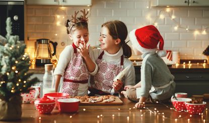 A happy mother with her two children, decorating Christmas cookies together in a festive, inviting kitchen.