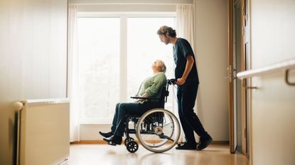 A stock photo of a male nurse pushing a patient in a wheelchair. 