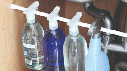 An under-sink storage space with a tension rod used to hang cleaning sprays