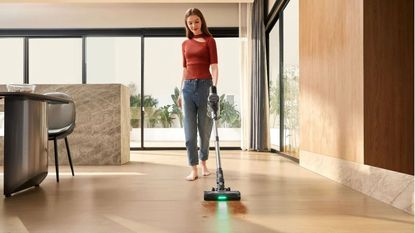 A barefoot lady vacuuming a hardwood floor Ultenic Vesla U12 which is emitting a green laser light