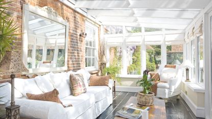 Light filled conservatory with light sofa and mirror on brick wall