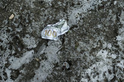 A $100 bill crumpled on a frosted, muddy ground.