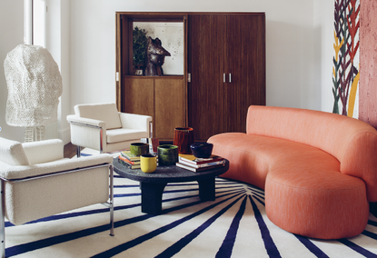 A living room with a curving orange sofa, and two white armchairs 