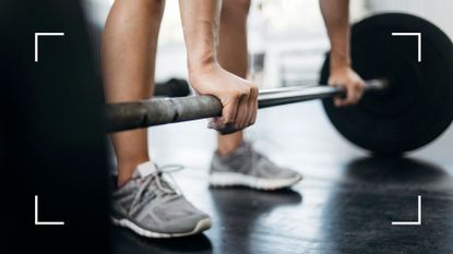 Woman bending down to pick up barbell from the floor as part of the 5x5 workout 