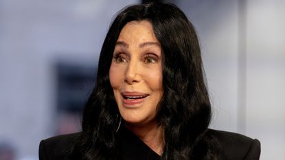 A headshot of Cher wearing a black jacket and looking to the left