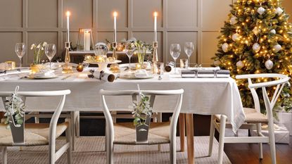 Wishbone style chairs around dining table set for Christmas. Four wreaths on a panelled feature wall and gold lit Christmas tree