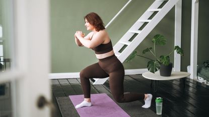 Woman exercising at home, she is in a lunge position with both knees bent and one foot behind the other