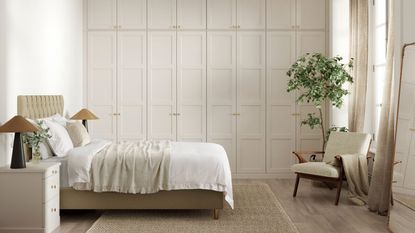 A neutral bedroom with large built in closets along the back wall with panelled walls. A double bed in front of them with two symmetrical night stands, a chair opposite 