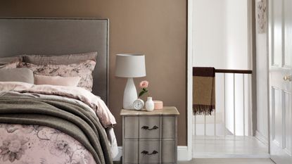 A bedroom with a brown wall and a bed with an upholstered headboard and pink floral bed linen