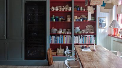 kitchen dining space with open shelving with red shiplap interior, books and crockery, dining table, to the left is mid blue cabinetry, Farrow &amp; Ball : Asger Mortensen, Wester Agency