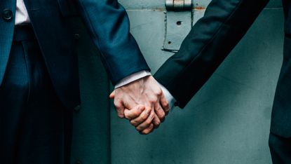 Two men (heads not showing) holding hands outside a prison door