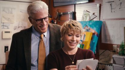 A father (Ted Danson as Charles) looks over the shoulder of his adult daughter (Mary Elizabeth Ellis as Emily) as she holds a set of photos, while the pair stand in a garage full of engineering tools, in episode 108 of A Man on the Inside.