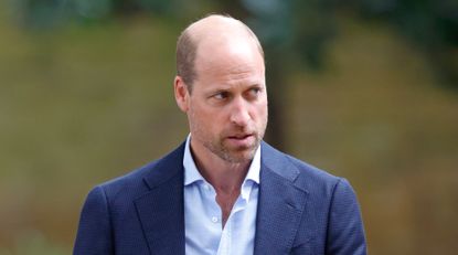 Prince William wears a blue suit with an open shirt and has beard stubble