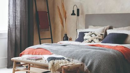 A bedroom with a bed dressed in grey and orange bedding