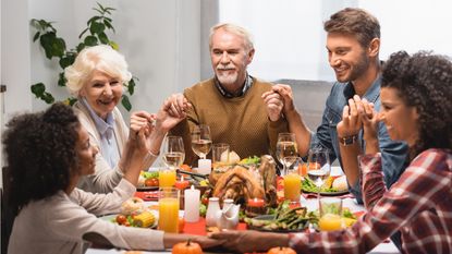 A multigenerational family holds hands and smiles at one another before diving into their turkey dinner.