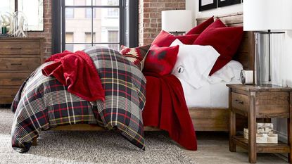 Side view of red and white bedding on a bed against an exposed brick wall.