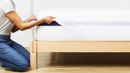 A woman pulling the Helix Plush Mattress Topper over the corner of a mattress. 