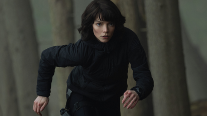 anya taylor joy in an all black outfit running through a forest in a still from the thriller the gorge