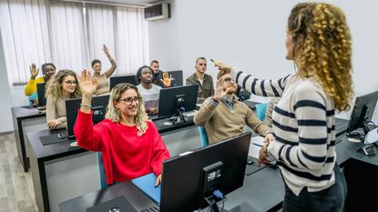 A seminar leader calls on someone in a class of students, many of whom have raised their hands.