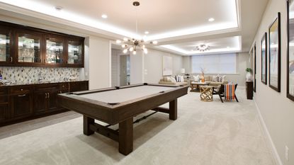 Beautiful basement entertaining room with LED lighting in tray ceiling and plush wooden billiards table