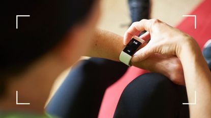 Woman looking down at a fitness tracker on her wrist, sitting on the floor of the gym