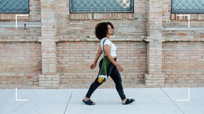 Woman wearing jeans and a t-shirt, carrying net bag with orange in the bottom, laughing and smiling walking along the pavement to represent how to lose weight without dieting