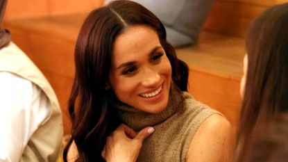 Meghan Markle speaks to women at an event wearing a sleeveless turtleneck and matching camel pants