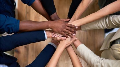 Several professionals stand in a circle and put their hands together in the center for teamwork. 