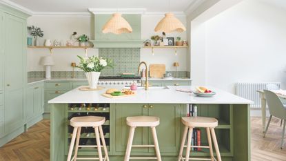 Kitchen with green kitchen cabinets and white worktop, with a matching kitchen island with wooden stools