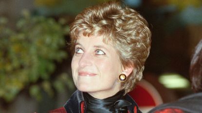 A headshot of Princess Diana wearing a red-and-black outfit and big black and gold Chanel button earrings looking to the left with a smile