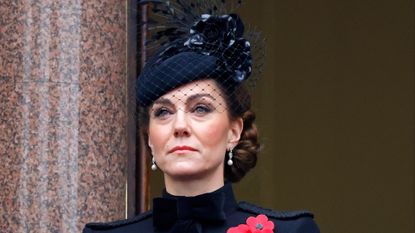 Kate Middleton wearing a black coat with poppy brooches and a black hat with a veil looking serious