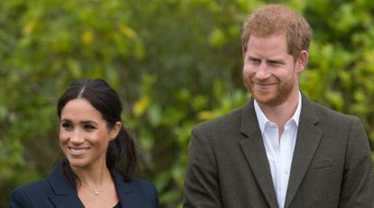 Meghan Markle wears a navy suit jacket with a black top and Prince Harry wears a white shirt with an overcoat