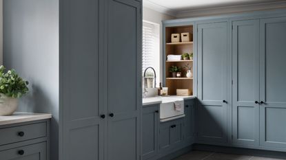 A utility room with floor-to-ceiling blue painted cabinets, and a large white farmhouse sink beneath a window