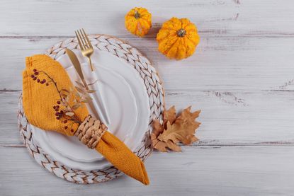 image of table setting for Thanksgiving with orange napkin and pumpkins near a plate