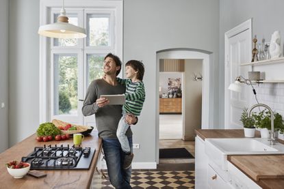 Father and son using tablet in kitchen looking at ceiling lamp