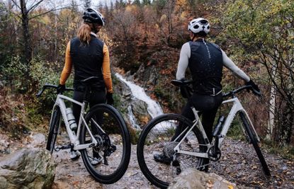 two gravel riders, one male and one female admiring a waterfall standing by their Riverside RCR grvael bikes