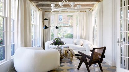 sunroom with check tile floors, boucle sofa and armchair, timber accent chair and white curtains