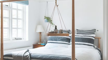 A white-painted guest room with a poster bed and striped bed linen