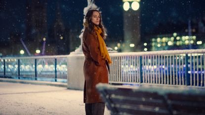 keira knightley wears an orange coat and stands on a snowy street in black doves