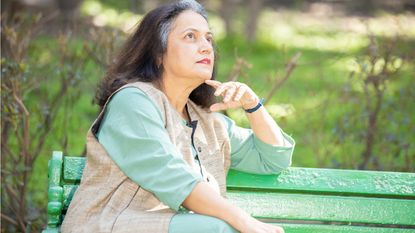 An older woman sits on a park bench and looks into the distance as she thinks.