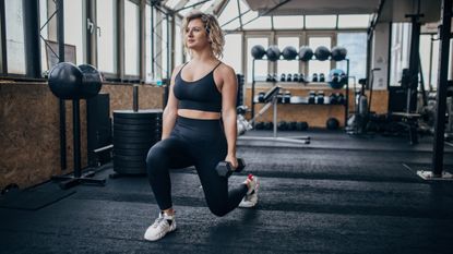 Woman in gym lunging while holding dumbbells