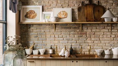 urban kitchen with exposed brick wall, copper countertop, brass hardware, plywood cabinets, single open shelf with objects, artwork, white tableware, deVOL