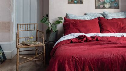 A wooden chair next to a bed dressed with red and white sheets against a cream wall.