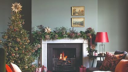 A living room decorated for Christmas with a Christmas tree and a garland draped over the lit fireplace adorned with hydrangeas