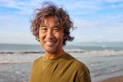 A relaxed surfer in his 50s on the beach smiles at the camera.