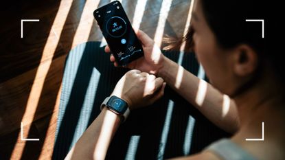 Woman looking at fitness tracker on wrist, sitting down on yoga mat at home, viewing workout metrics after considering are fitness trackers worth it in 2024