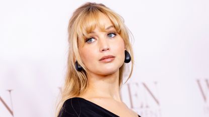 Jennifer Lawrence on a red carpet wearing a black off the shoulder dress with bottega veneta earrings