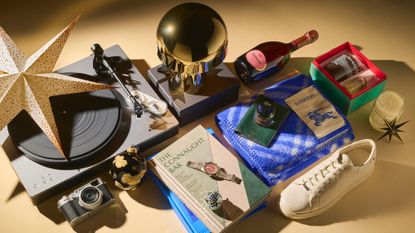 A selection of items from the Marie Claire Christmas Gifts for Him gift guide which include a turntable, gold lamp, champagne bottle, books, a Burberry scarf, Le labo candle and more