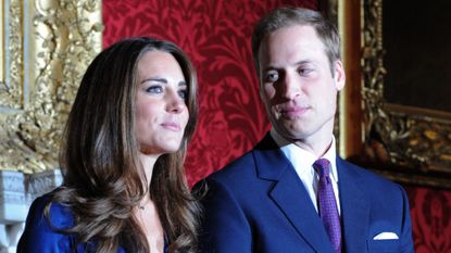 Kate Middleton wears a blue dress and has long curly hair as Prince William looks at her announcing their engagement