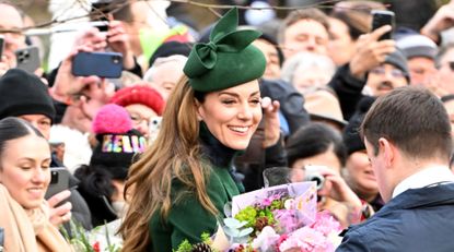 Kate Middleton wears a green hat and coat as she&#039;s surrounded by royal fans who have given her bunches of flowers at Sandringham